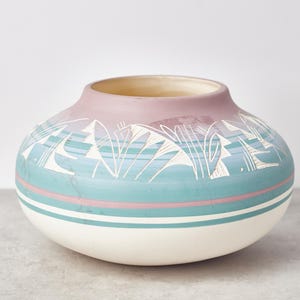 Puede incluir: Una maceta de cerámica blanca con un diseño geométrico rosa y azul. La maceta tiene una base ancha y una forma redondeada.