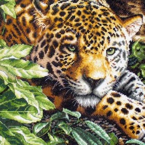 Puede incluir: Un detallado bordado de un jaguar, con pelaje dorado y manchas negras, y ojos verdes. El gran felino está parcialmente oculto por un exuberante follaje verde, creando una escena de jungla. La obra de arte muestra puntadas intrincadas y una representación realista.