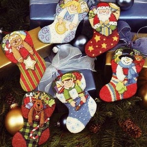 Puede incluir: Seis calcetines navideños bordados con diversos diseños. Los calcetines presentan imágenes de Papá Noel, un muñeco de nieve, un ángel, un hombre de jengibre, un reno y un elfo. Los colores son rojo, verde, azul y blanco, con detalles dorados.