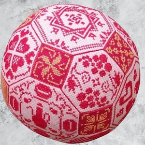 May include: A pink and red sphere with a geometric pattern, made of fabric and stitched together. The sphere is covered in a variety of small, colourful designs.