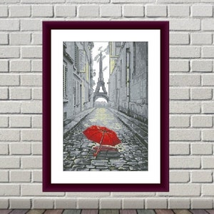 Puede incluir: Un paraguas rojo yace en una calle adoquinada de París, con la Torre Eiffel visible en la distancia.