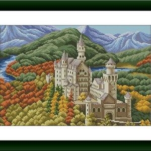 Peut inclure: Une broderie au point de croix représentant un château en pierre à plusieurs tours niché dans un paysage d'arbres aux couleurs automnales, une rivière bleue sinueuse et des montagnes aux tons violets, encadrée d'un cadre vert foncé.