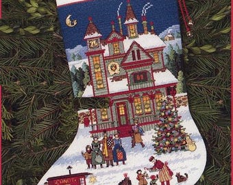 May include: Embroidered Christmas stocking with a winter scene featuring a large house, a Christmas tree, and figures in the snow. The name "Daniel" is stitched at the top. A red candy shop wagon is also depicted.