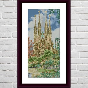 May include: A framed cross-stitch embroidery depicting a detailed view of a large, ornate church with multiple towers. The church is surrounded by green trees and a small pond. The sky is blue with white clouds.