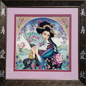 May include: Framed cross-stitch artwork featuring a geisha holding a fan. The geisha is dressed in a colorful kimono with floral patterns. The background includes a landscape with a river, cherry blossoms, and wisteria. The frame has Japanese characters.