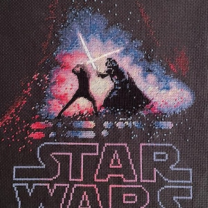 Peut inclure: Broderie au point de croix représentant une scène de Star Wars avec deux personnages en duel au sabre laser. Les personnages sont en silhouette sur un fond de lumière pixélisée rouge, bleue et blanche. Le logo Star Wars est brodé en dessous.