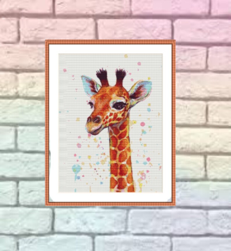 Op de afbeelding: Een ingelijst kruissteekpatroon van een giraffe met een witte achtergrond en kleurrijke verfspatten. De giraffe is bruin en oranje met een lange nek en grote oren.