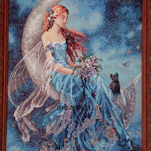 May include: Cross-stitch artwork of a fairy with red hair and a blue dress, seated on a crescent moon. She holds flowers and is accompanied by a black cat and a butterfly. The background is a blue sky.