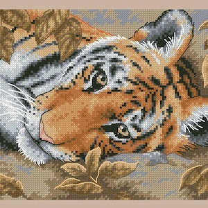 Puede incluir: Patrón de punto de cruz de un cachorro de tigre con rayas naranjas y negras, acostado entre hojas marrones. La cara del tigre está detallada con ojos negros y bigotes blancos, sobre un fondo beige.