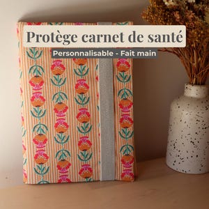 Könnte beinhalten: Ein Set aus drei Keramikbechern mit gesprenkelter, cremefarbener Glasur. Jeder Becher zeigt ein handgemaltes Blumendesign in Blau-, Grün- und Gelbtönen. Die Becher haben eine einfache, abgerundete Form und einen Griff.