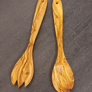 Op de afbeelding: Een set van twee houten saladebestek gemaakt van olijfhout. De bestekken hebben een natuurlijke houtkleur en zijn ontworpen met een lepel en een vork.