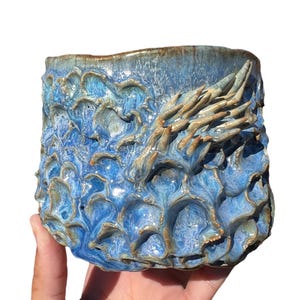May include: A blue and brown ceramic planter with a textured surface and a raised design. The planter has a unique, organic shape.