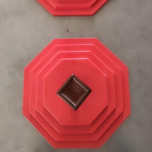 May include: Two red octagonal tiered cake stands with a brown square knob on top. The stands are made of plastic and have a glossy finish.