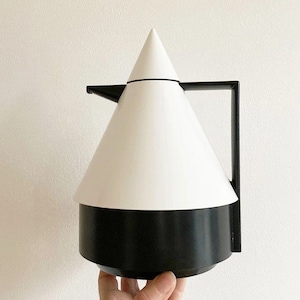 Può includere: Una caraffa termica bianca e nera con forma conica e manico. La caraffa è in plastica e ha una base nera.