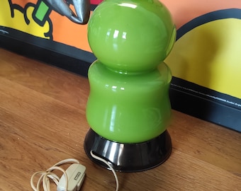 May include: A green glass table lamp with a round base and a cord with a switch. The lamp is on a wooden surface.