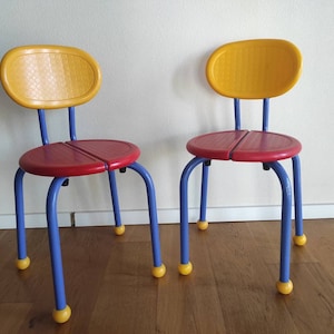May include: Two colorful children's chairs with yellow, red, and blue plastic seats and blue metal legs. The chairs have round yellow plastic feet.