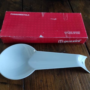 Peut inclure: Repose-cuillère en céramique blanche avec le texte "Guzzini" sur la boîte rouge dans laquelle il était livré. La boîte indique également "Campione Omaggio non destinato alla vendita", ce qui se traduit par "Échantillon gratuit non destiné à la vente".