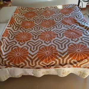 Puede incluir: Un cubrecama de color marrón y blanco con un diseño geométrico que presenta flores estilizadas. El cubrecama está hecho de una tela suave y texturizada.