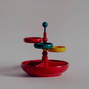 Könnte beinhalten: Eine dreistufige Schmuckschale in Rot, Grün und Gelb mit einem runden Boden und drei kleineren Schalen. Die Schale ist aus Kunststoff und hat ein Retro-Design.