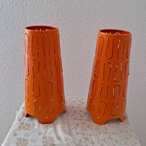 May include: Two orange metal lampshades with a unique cut-out design. The lampshades are cone-shaped and have a scalloped bottom edge.