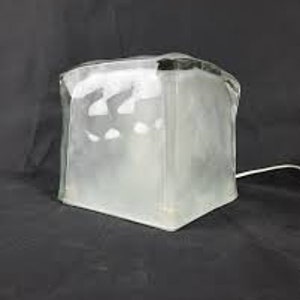 Puede incluir: Una lámpara de vidrio esmerilado con forma cuadrada y superficie texturizada. La lámpara tiene un cable blanco.