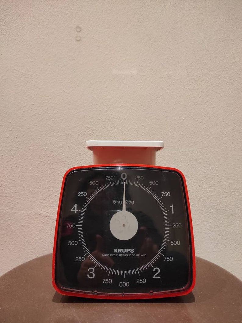 Puede incluir: Una b&aacute;scula de cocina roja y negra con un dial blanco y una cara negra. La b&aacute;scula marca 5 kg 25g. La b&aacute;scula est&aacute; fabricada por Krups y est&aacute; fabricada en la Rep&uacute;blica de Irlanda.