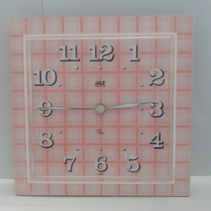 May include: A square pink and white checked clock with black numbers and hands. The clock face says "JAZ QUARTZ" and "Paris".