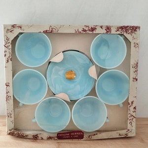 Puede incluir: Un juego de seis tazas de café de vidrio azul claro y un platillo a juego en una caja blanca con un patrón floral. La caja tiene el texto "OPALINE DURALEX TASSES A CAFE" impreso en la parte inferior.