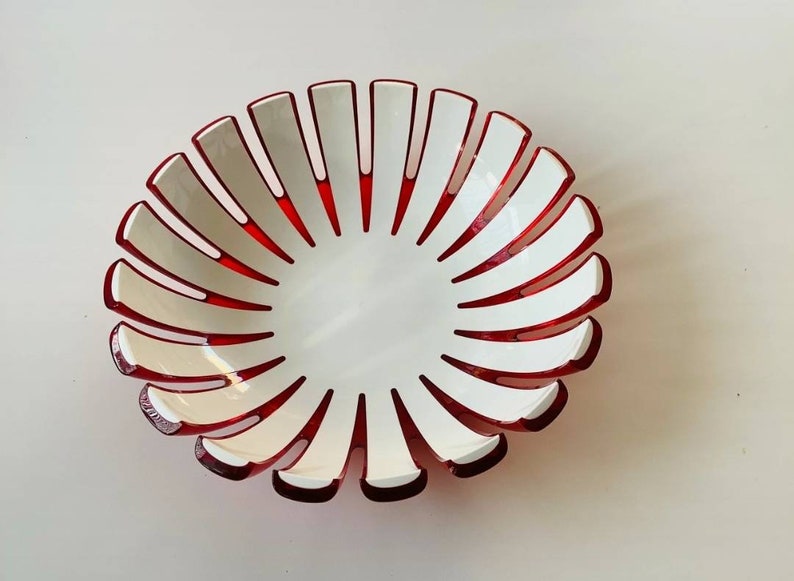 K&ouml;nnte beinhalten: Eine dekorative Schale mit einzigartigem Design. Die Schale hat ein wei&szlig;es Innen- und Au&szlig;endesign mit roten Akzenten. Der Rand weist wei&szlig;e, bl&uuml;tenblattartige Formen mit roten Details auf, die ein ansprechendes Muster bilden. Diese Schale eignet sich zum Servieren oder Dekorieren.