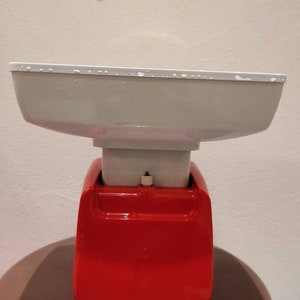 Puede incluir: Una b&aacute;scula de cocina roja y blanca con un cuenco blanco en la parte superior. La b&aacute;scula tiene una base roja y una parte superior blanca con un peque&ntilde;o bot&oacute;n en la parte delantera.