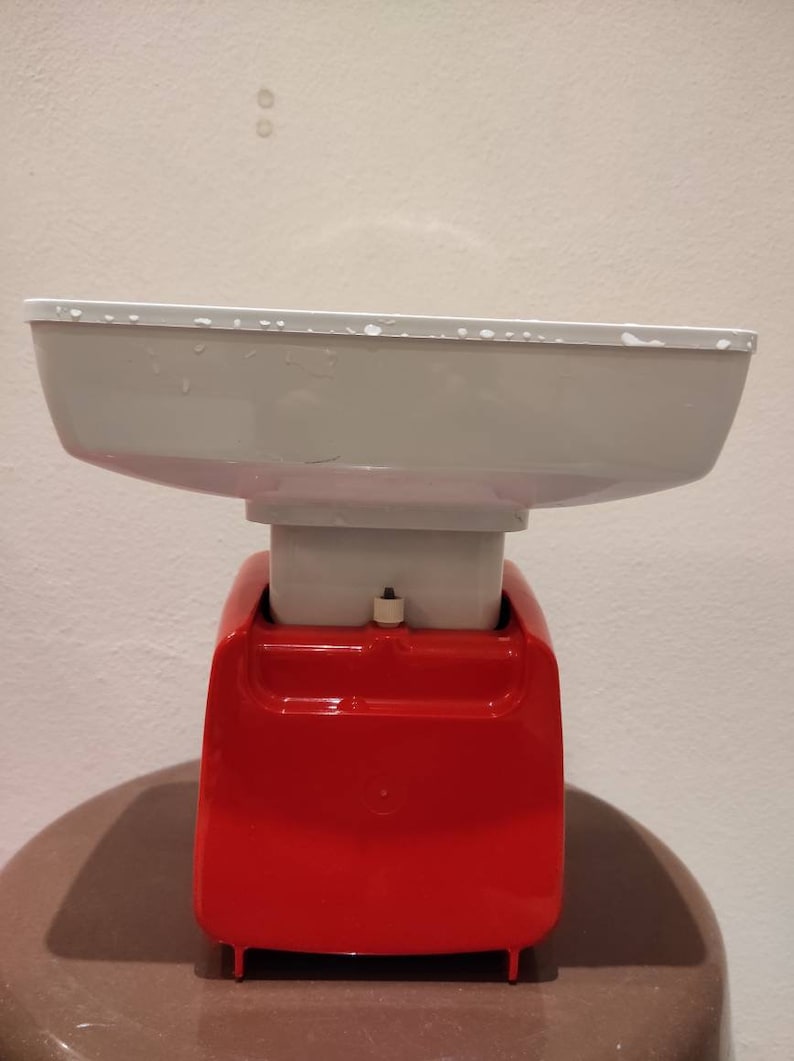 Puede incluir: Una b&aacute;scula de cocina roja y blanca con un cuenco blanco en la parte superior. La b&aacute;scula tiene una base roja y una parte superior blanca con un peque&ntilde;o bot&oacute;n en la parte delantera.