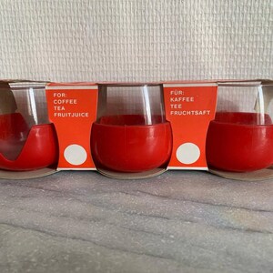 May include: Set of four red and clear glass cups with a white label that reads "FOR: COFFEE TEA FRUITJUICE" and "FÜR: KAFFEE TEE FRUCHTSAF"