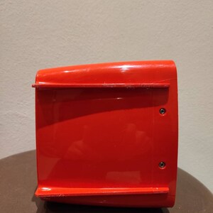 Puede incluir: Un contenedor de almacenamiento de pl&aacute;stico rojo brillante con dos peque&ntilde;os tornillos negros en el lateral.