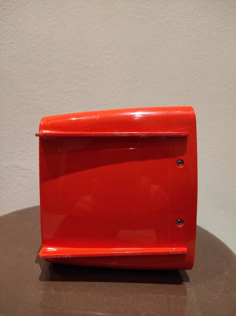 Puede incluir: Un contenedor de almacenamiento de pl&aacute;stico rojo brillante con dos peque&ntilde;os tornillos negros en el lateral.