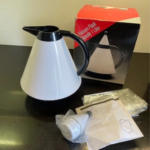 Può includere: Una caraffa termica bianca con manico e beccuccio neri. La caraffa ha una capacità di 1 litro e viene fornita con un coperchio e le istruzioni. La scatola è rossa e nera con il testo "Caraffa termica Capacità 1 Litro".