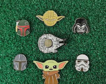 May include: A set of seven Star Wars enamel pins featuring characters and vehicles from the franchise. The pins include Yoda, Darth Vader, Boba Fett, a Mandalorian, Baby Yoda, a Stormtrooper, and the Millennium Falcon.