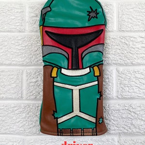 May include: A green, brown, and gray golf club head cover with a Star Wars Boba Fett design. The head cover is labeled "driver".