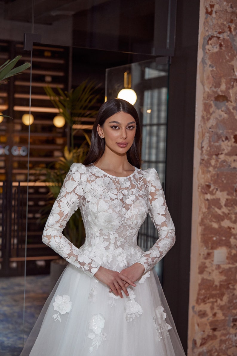 modest wedding dress, floral lace top with long sleeves, lace sleeves are puffed on the shoulders, boat neckline, corset with built-in bra and ribbon fastening on the back, a line tulle skirt is adorned with lace appliques on the top