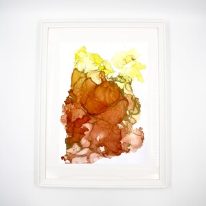 Puede incluir: Impresión de arte abstracto con un esquema de color amarillo, naranja y marrón. La impresión presenta una gran forma orgánica en el centro, rodeada de formas más pequeñas.