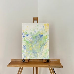 Pode incluir: Pintura abstrata em tela com um padr&atilde;o de pintura azul, verde e amarelo em espiral. A pintura &eacute; exibida em um cavalete.