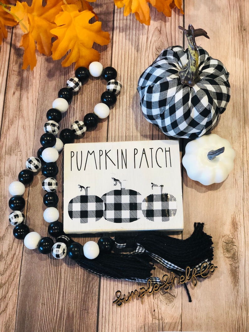 May include: Black and white checkered pumpkin patch sign with three pumpkins, a black and white checkered pumpkin, a white pumpkin, and a black and white beaded garland. The sign says "Pumpkin Patch".