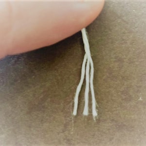 May include: Close-up of four white cotton threads hanging from a finger.