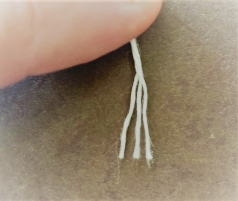 May include: Close-up of four white cotton threads hanging from a finger.