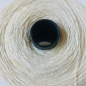 May include: A spool of natural white cotton thread wound around a black plastic center.