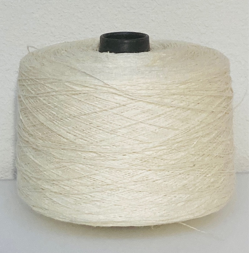 May include: A large spool of natural white yarn, wound tightly and ready for use in crafting projects.