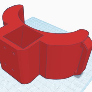 Puede incluir: Un soporte de plástico rojo impreso en 3D con una abertura cuadrada y una sección curva. El soporte tiene varios agujeros pequeños en el lateral.
