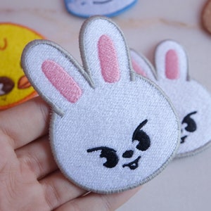 May include: White bunny face patch with pink inner ears and black embroidered eyes and mouth. The patch has a gray border. Other animal face patches are visible in the background.