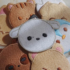 Puede incluir: Una colección de parches bordados con caras de animales. Los parches incluyen un tigre marrón, un perro beige, una oveja blanca y un pingüino azul. Cada parche tiene costuras detalladas y un diseño de dibujos animados.