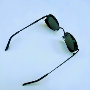 May include: Black round sunglasses with a metal frame. The sunglasses have a dark lens and are on a white background.