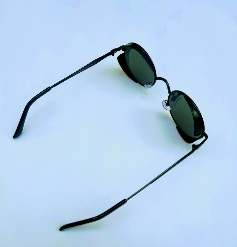 May include: Black round sunglasses with a metal frame. The sunglasses have a dark lens and are on a white background.